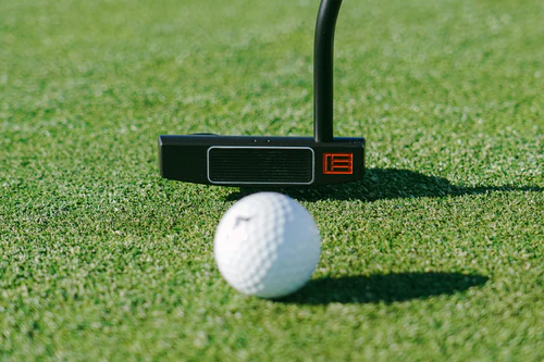 Front side of black putter hitting ball