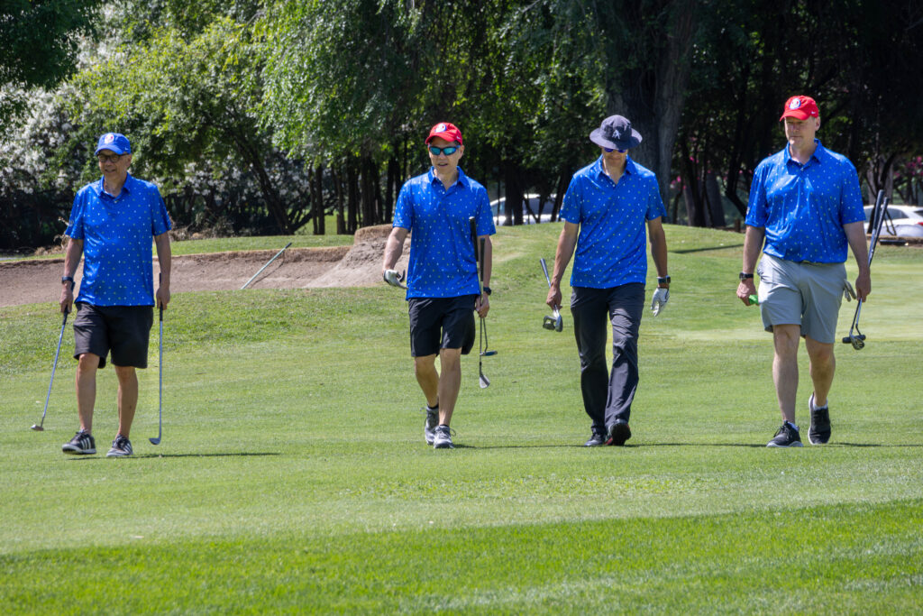 A group of golfers walking along the fairway. They are all wearing the same blue polo shirts, commemorating the 100th anniversary.