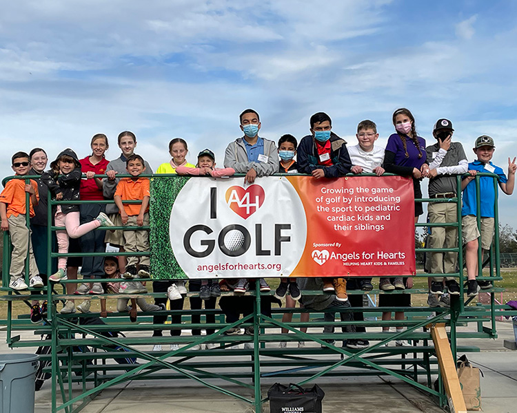Group of I LOVE Golf Participants on bleachers behind banner for Angels for Hearts Organization