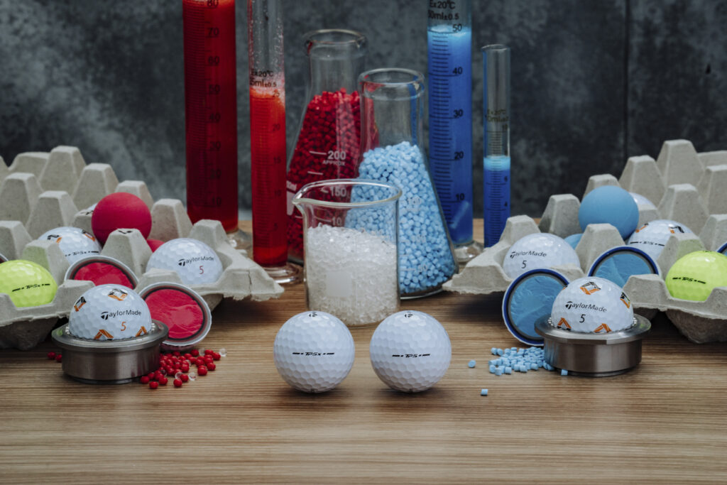 Chemistry lab photo, cylinders with red and blue filing. Two golf balls in the center on the image, and a few cut in half golf balls surrounding.