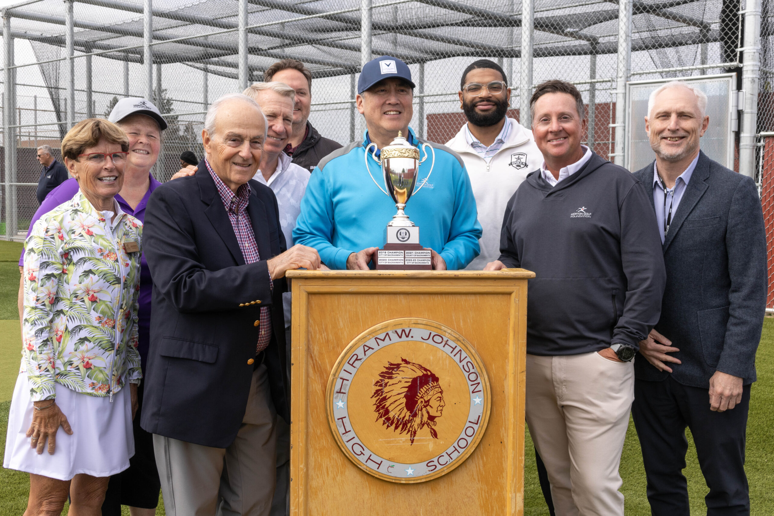 A group photo of the city council members and the Morton Golf Foundation members at the ribbon cutting. They are standing in front of a podium with Hiram Johnson's logo on it.