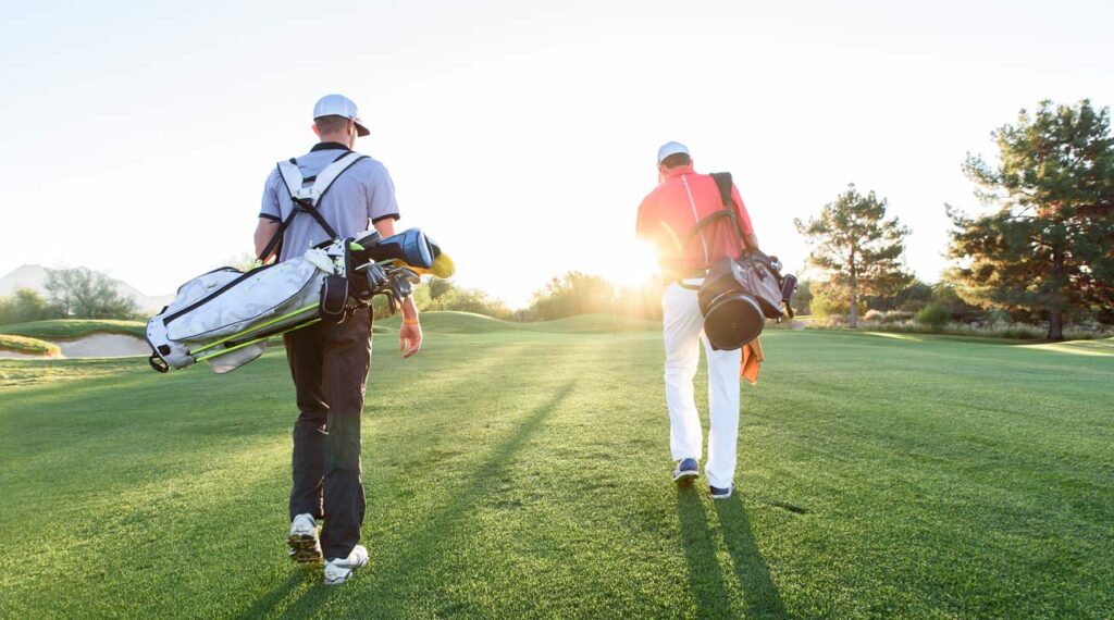 Two Golfers walking on golf course with sun setting 