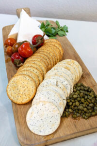 Photo of cheese tomato cracker and capers on a serving board