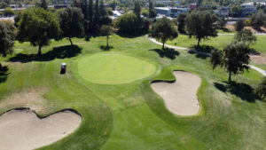 A birds-eye view of the #8 hole green on the Alister MacKenzie golf course. There are two bunkers around the green and a golf cart is driving on the rough just off the green.