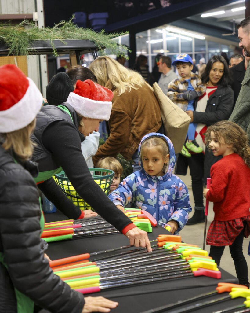 A child watches as one of Santa's helpers is grabbing a putter to give to them.