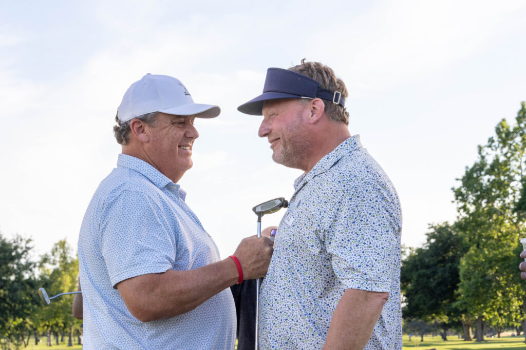 A closeup of two golfers at the 2025 Morton Golf Foundation Putting Party. They are smiling while one holds a putter to the others chest.