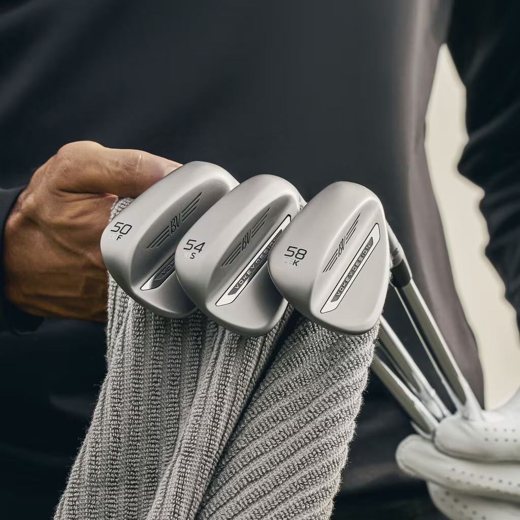 Three SM11 wedges held by a golfer while they wipe them with a towel.