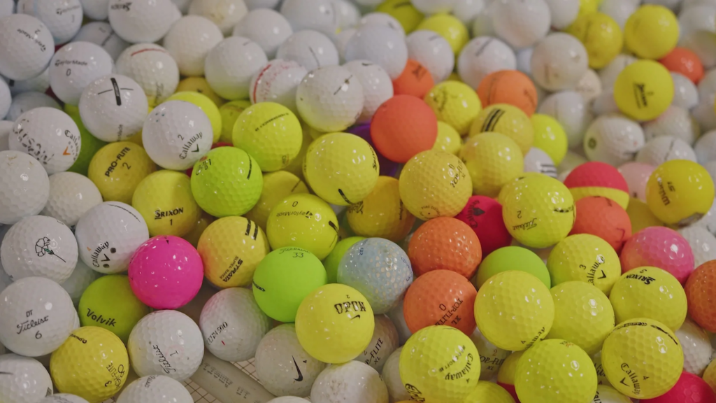 A close up of a large pile of golf balls from many different brands. The balls are various colors including white, neon yellow, pink, matte red, green, and purple.