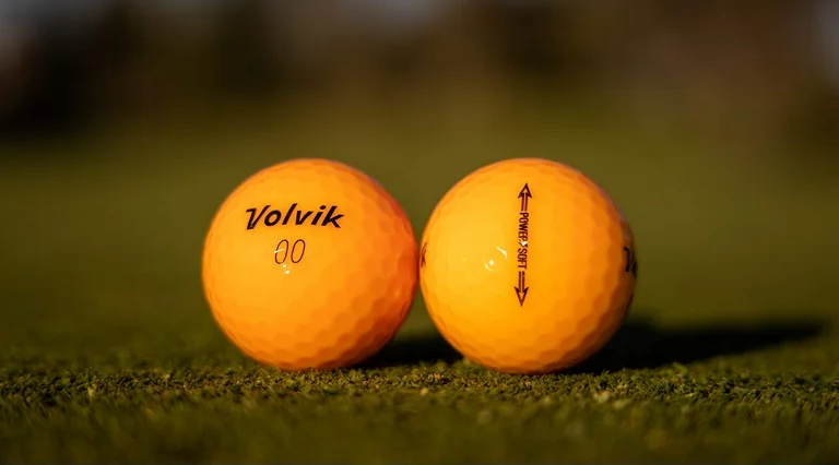 A close up of two orange Volvik balls next to each other on grass.