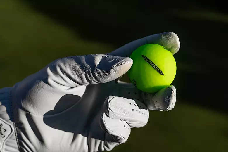 A gloved hand holds a neon green Callaway golf ball.