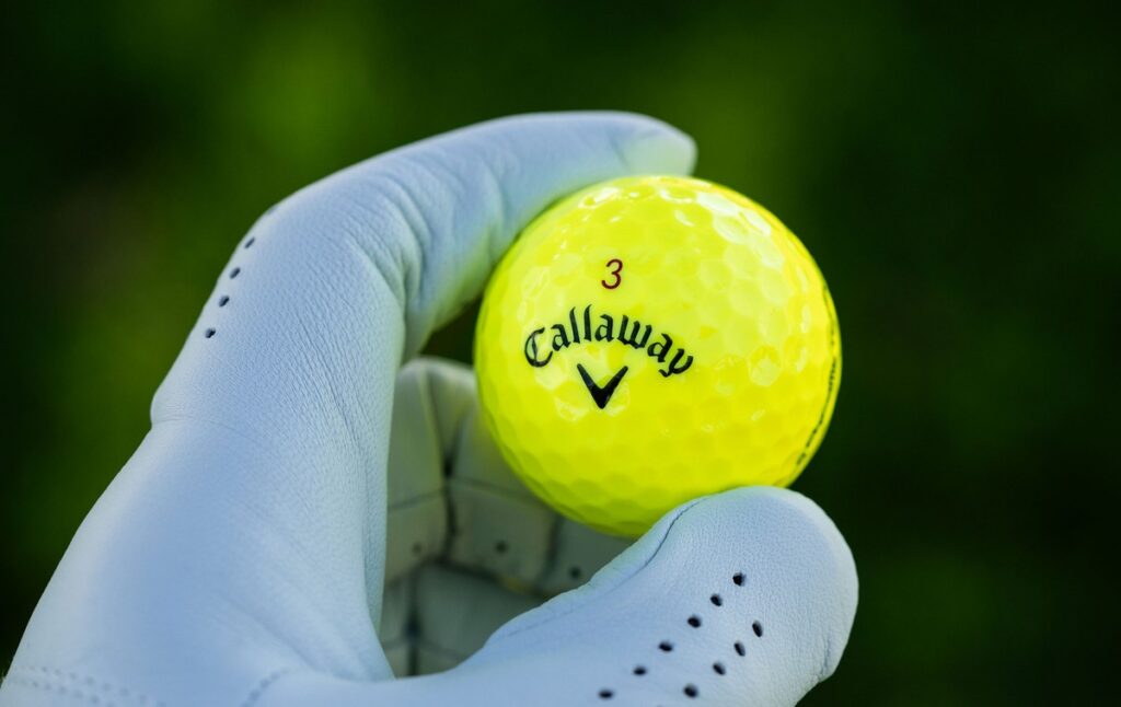 A gloved hand holds a neon yellow Callaway golf ball.