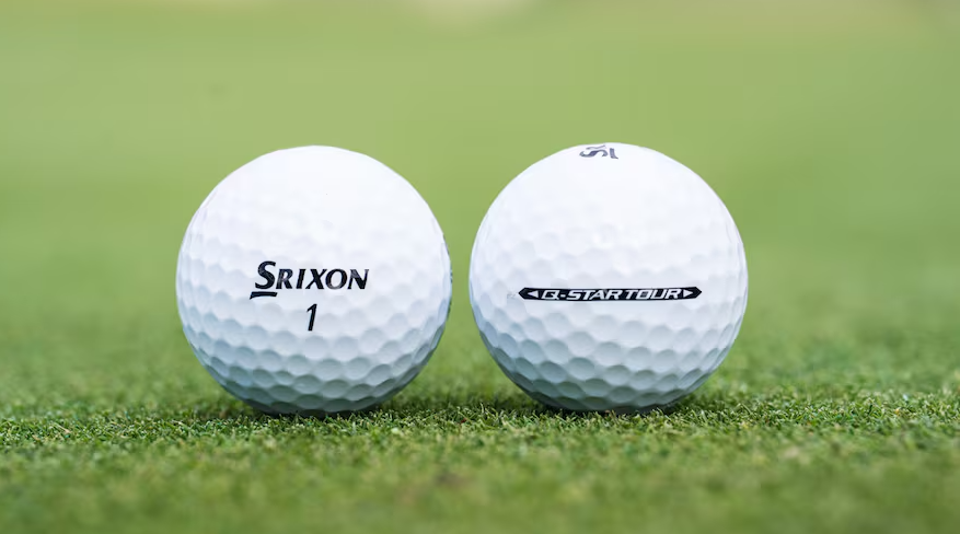Two white Srixon golf balls lined up next to each other on grass.