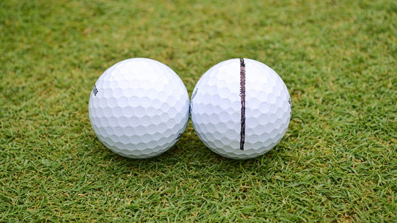 Two golf balls side by side, one with a line drawn in sharpie on it, one without.
