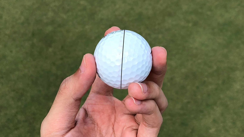 A hand holding a golf ball with a straight alignment line printed onto it.