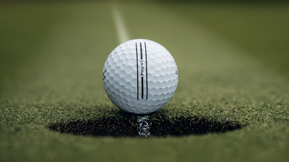 A ProV1 golf ball sits at the edge of a golf hole, along a line leading from the distance to the hole. It has a ProV1 alignment aid on the ball.