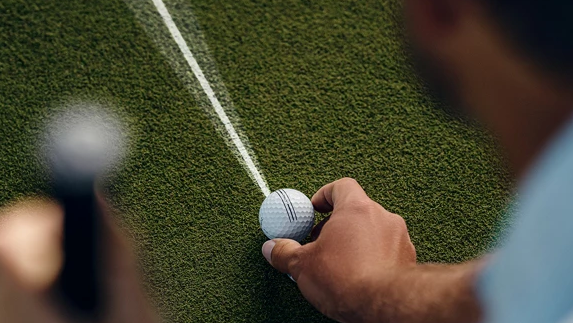 A man lines up a ProV1 golf ball along an alignment line.