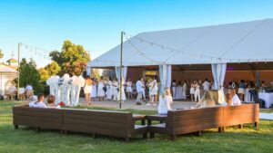 Daytime event at Creekside at Haggin Oaks with a large white tent, guests dressed in white, lounge seating on the lawn, and string lights overhead.