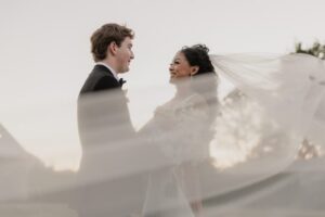 Bride and groom smiling at each other during an outdoor wedding at Haggin Oaks, with the bride’s veil flowing in the breeze.