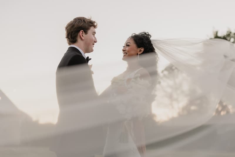 Bride and groom smiling at each other during an outdoor wedding at Haggin Oaks, with the bride’s veil flowing in the breeze.