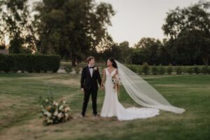 Bride and groom walking hand in hand across a golf course at Haggin Oaks, with the bride’s long veil trailing behind and bouquet in hand.