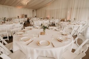 Elegant indoor wedding reception setup at Haggin Oaks with round tables, white linens, floral centerpieces, and neatly arranged place settings inside a draped event tent.