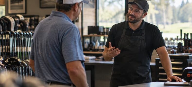 Golf club repair technician talking with a customer inside a golf shop